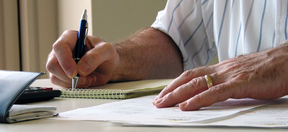 Man writing on notepad wiht check book and calculator